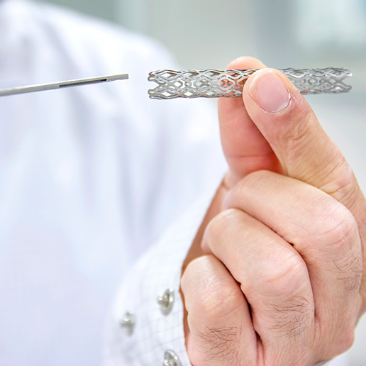 Man in lab coat holding heart stent in his hand.
