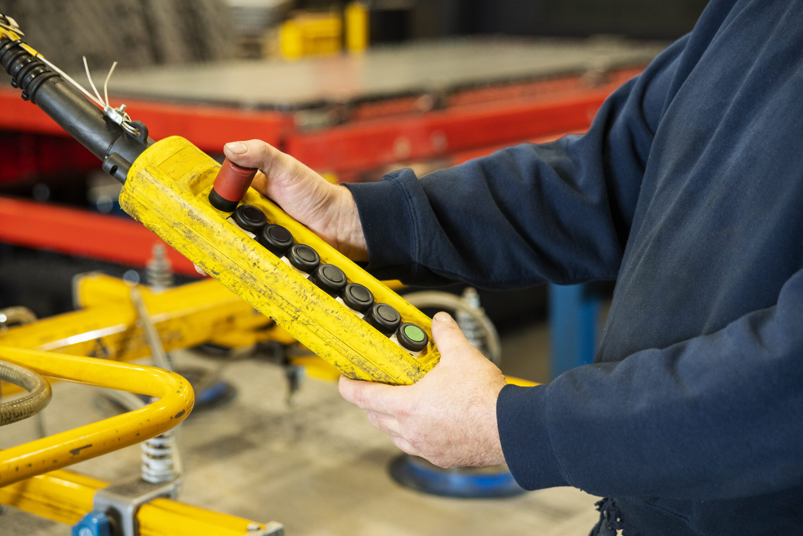 A crane operator's hands and chest holding a pendant controller that operates a crane